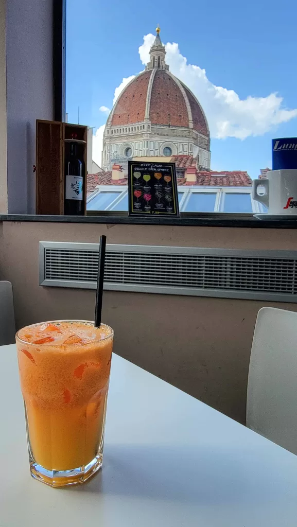 A glass of orange juice on a table in a cafe with a view of the Duomo in Florence