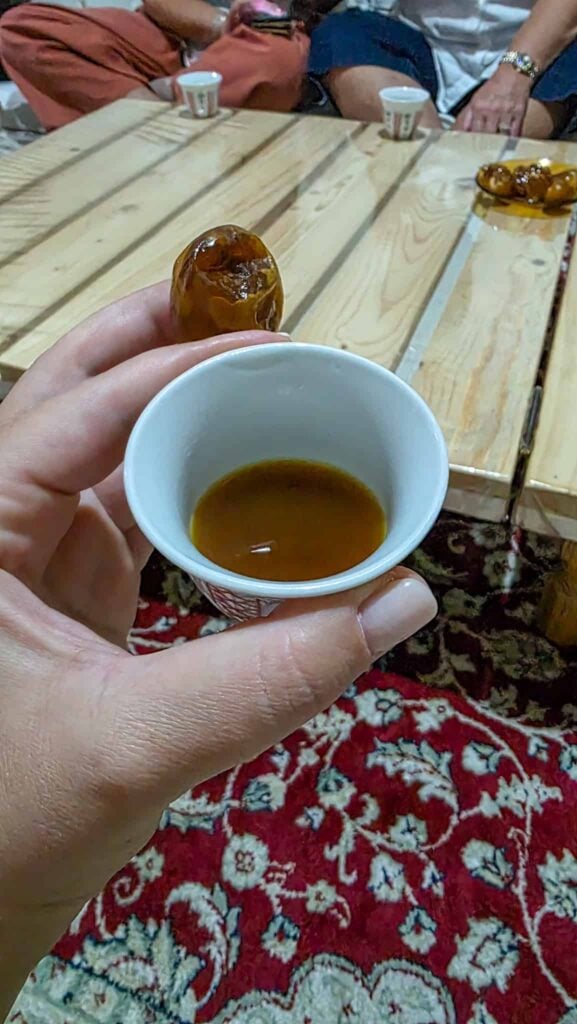 the author holding a cup of arabic coffee and a date